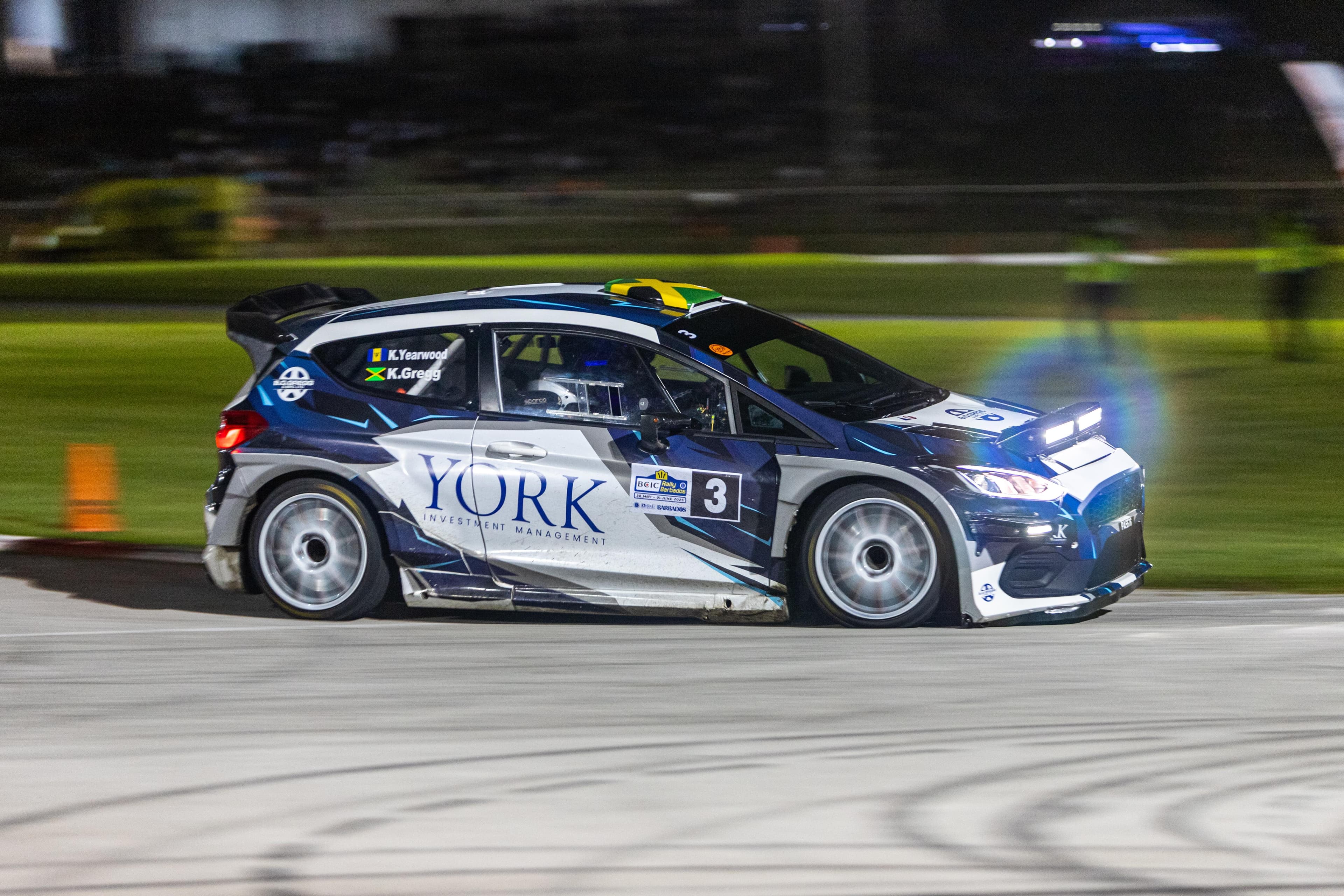 Rally car mid-jump over a hill on a tropical road